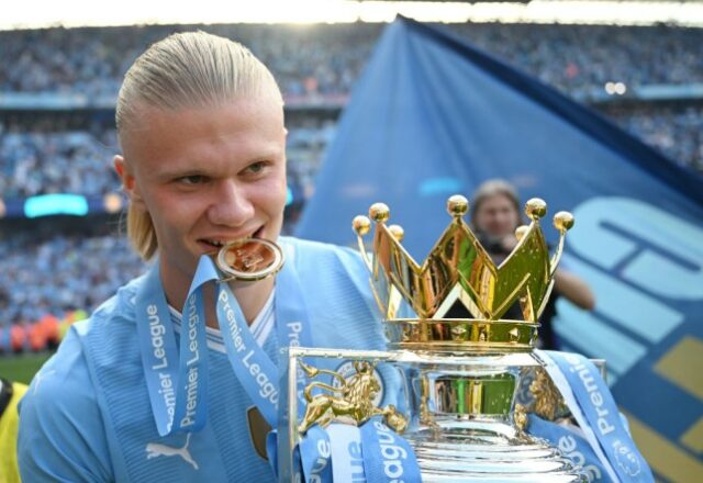 Erling Haaland, do Manchester City, morde a medalha do vencedor ao comemorar com o troféu da Premier League 