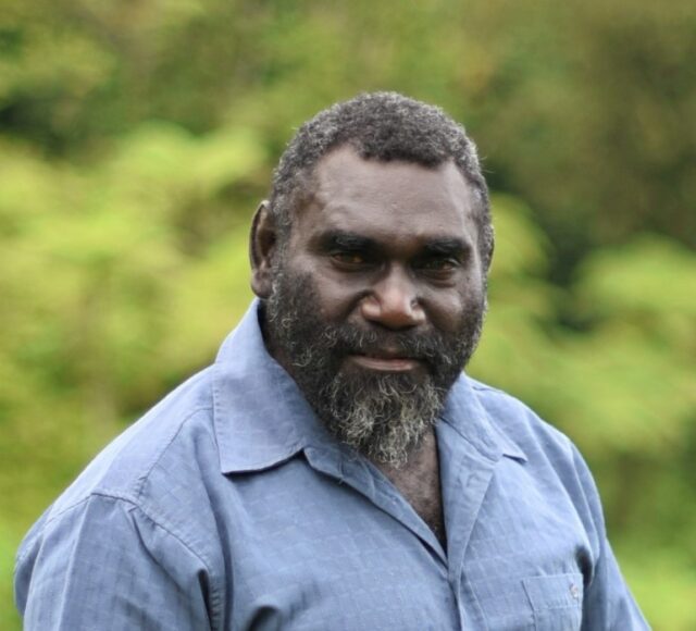 Uma fotografia da cabeça e dos ombros do presidente de Bougainville, Ishmael Toroama.  Ele está vestindo uma camisa azul clara com gola aberta.