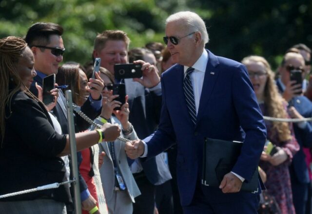 Joe Biden caminha ao longo de uma fila de apoiadores, que estão atrás de uma barricada do lado de fora, alguns apontando celulares com câmeras para o presidente.