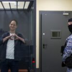 O repórter do Wall Street Journal, Evan Gershkovich, que está sob custódia sob acusação de espionagem, faz um gesto em forma de coração dentro de um recinto para réus antes de uma audiência em Moscou, Rússia, 23 de abril.