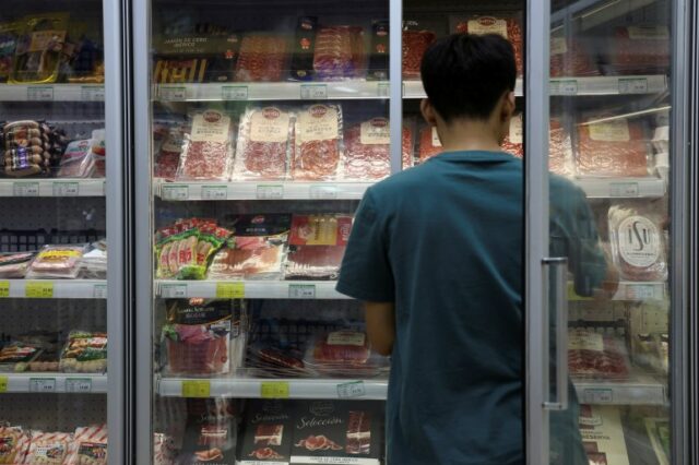 Um membro da equipe estoca um freezer onde são exibidos carne de porco e outros produtos cárneos