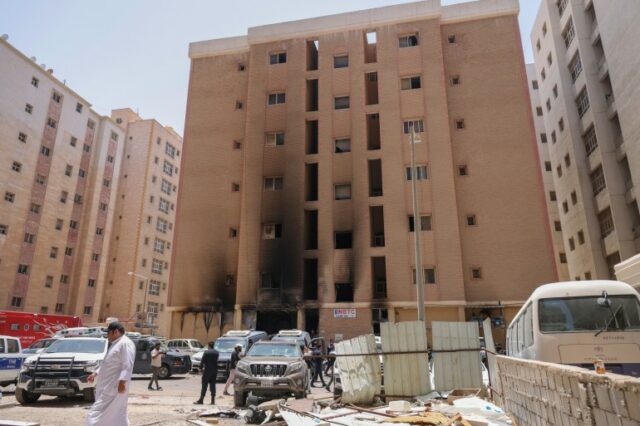 Pessoas passam por um prédio que foi engolido por um incêndio, na Cidade do Kuwait