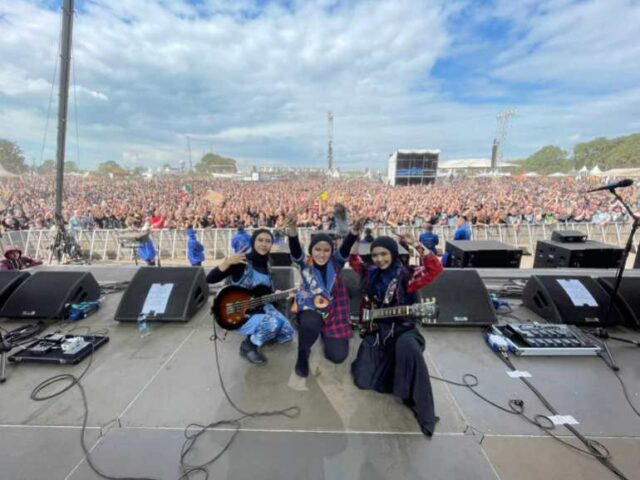 O trio no palco do Wacken Open Air, festival na Alemanha/ Eles estão posando no palco.  Há uma multidão enorme atrás deles.