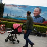 As pessoas passam por um pôster do falecido líder chinês Deng Xiaoping, que lançou o país em sua