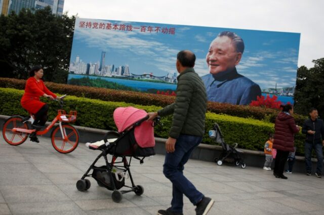 As pessoas passam por um pôster do falecido líder chinês Deng Xiaoping, que lançou o país em sua 