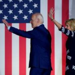 Joe e Jill Biden acenando para a multidão enquanto caminham pelo palco.  Há uma grande bandeira dos EUA atrás deles.