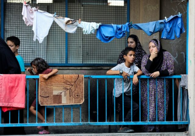 Palestinos ficam em uma varanda enquanto outros se reúnem no local de um ataque aéreo israelense contra uma escola da ONU que abriga pessoas deslocadas