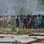 Um manifestante atira um objeto enquanto os manifestantes entram em confronto com a Guarda de Fronteira de Bangladesh (BGB) e a polícia do lado de fora da televisão estatal de Bangladesh, enquanto a violência irrompe em todo o país após protestos anti-cotas de estudantes