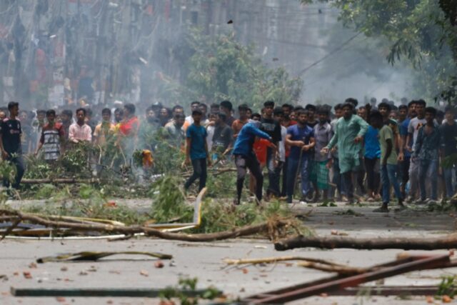 Um manifestante atira um objeto enquanto os manifestantes entram em confronto com a Guarda de Fronteira de Bangladesh (BGB) e a polícia do lado de fora da televisão estatal de Bangladesh, enquanto a violência irrompe em todo o país após protestos anti-cotas de estudantes