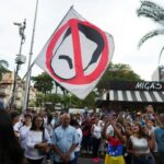 Um manifestante no meio de uma multidão segura uma bandeira que mostra um desenho animado do rosto bigodudo de Nicolás Maduro riscado.