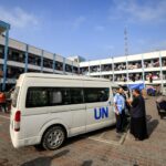 Um homem fala com um funcionário da Agência das Nações Unidas de Assistência e Obras para os Refugiados da Palestina (UNRWA) do lado de fora de um de seus veículos estacionados no playground de uma escola administrada pela UNRWA que foi convertida em um