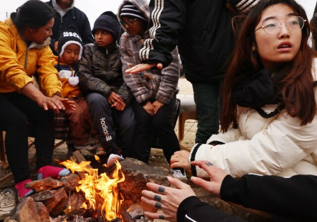 Migrantes da China e do Equador reúnem-se em torno de uma fogueira num acampamento improvisado depois de cruzarem a fronteira para os EUA.