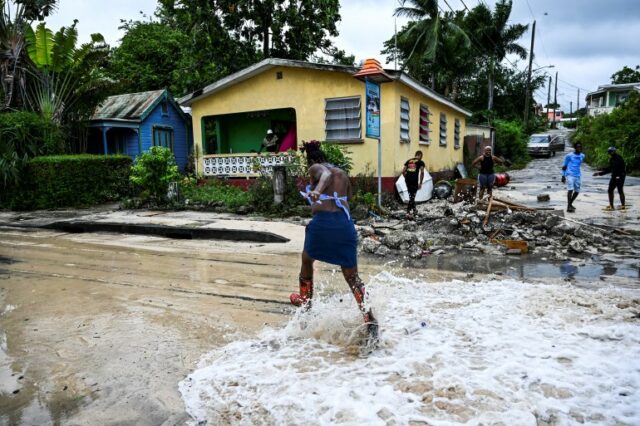 Uma mulher corre para evitar a entrada de água do mar em uma rua em St James, Barbados