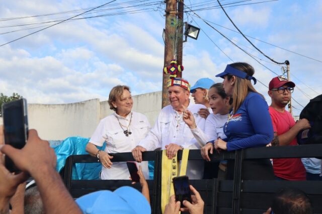 Edmundo González Urrutia, com cocar tradicional, desfila pelas ruas na traseira de um caminhão.