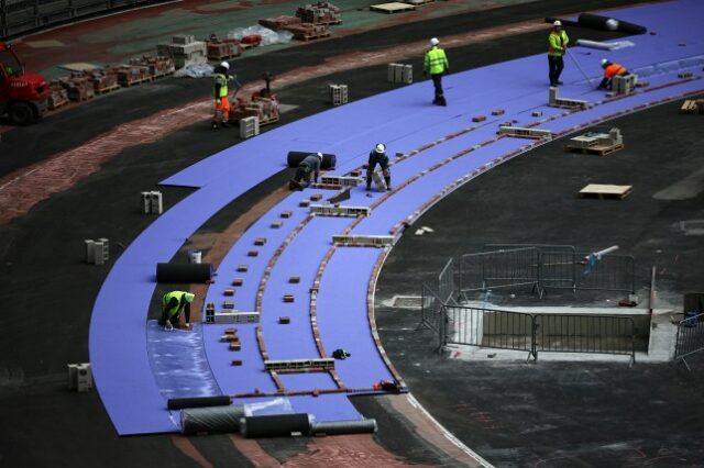 Trabalhadores instalam pistas de atletismo roxas durante obras de reforma para adaptar o Stade de France antes dos Jogos Olímpicos de Paris 2024