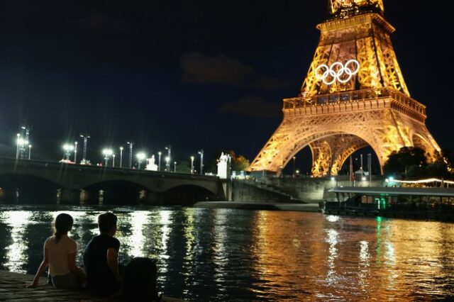 Espectadores veem a Torre Eiffel e os anéis olímpicos ao longo do rio Sena em 21 de julho de 2024