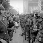 Uma foto de arquivo em preto e branco mostra policiais armados e com capacetes e manifestantes alinhados, frente a frente em uma ampla avenida de Chicago.