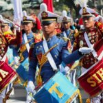 Bandas militares marchando. Eles têm tambores e faixas coloridas.