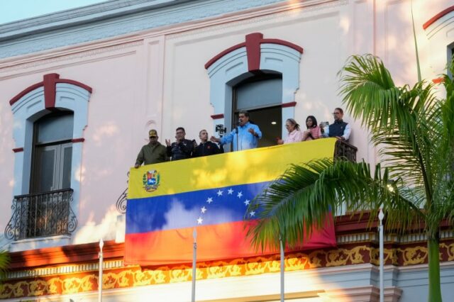 Nicolás Maduro cumprimenta apoiadores em uma varanda coberta com uma bandeira no palácio presidencial de Miraflores, em Caracas.