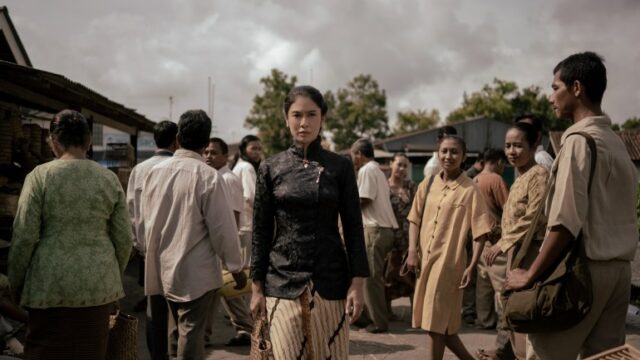 Uma foto do drama Netlfix Gadis Kretek (Cigarette Girl).  Mostra Dasiyah, o personagem interpretado por Dian Sastrowardoyo, saindo da multidão.  Ela parece determinada.