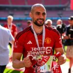 Amrabat segurando o troféu da FA Cup e vestindo um uniforme do Man United.