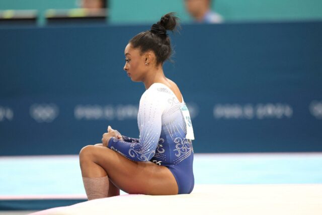 Simone Biles sentada no chão nas Olimpíadas de 2024