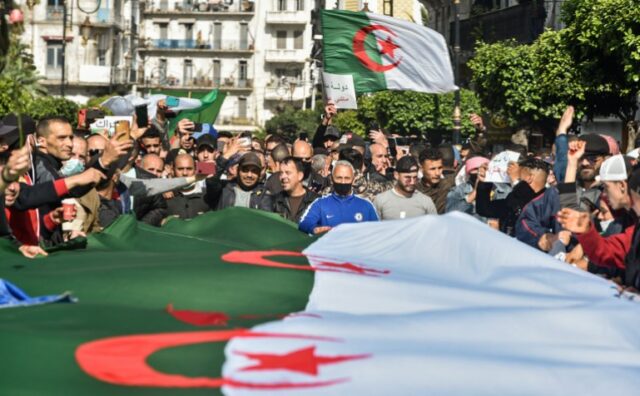 Argelinos agitam bandeiras nacionais durante um protesto antigovernamental na capital Argel, em 5 de março de 2021. - Milhares de pessoas manifestaram-se em Argel e outras cidades do país, confirmando a remobilização do movimento de protesto Hirak novamente nas ruas desde o segundo aniversário da revolta de 22 de fevereiro. (Foto de RYAD KRAMDI / AFP)