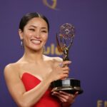 Anna Sawai segurando seu Emmy. Ela está usando um vestido de noite vermelho. Ela está sorrindo.