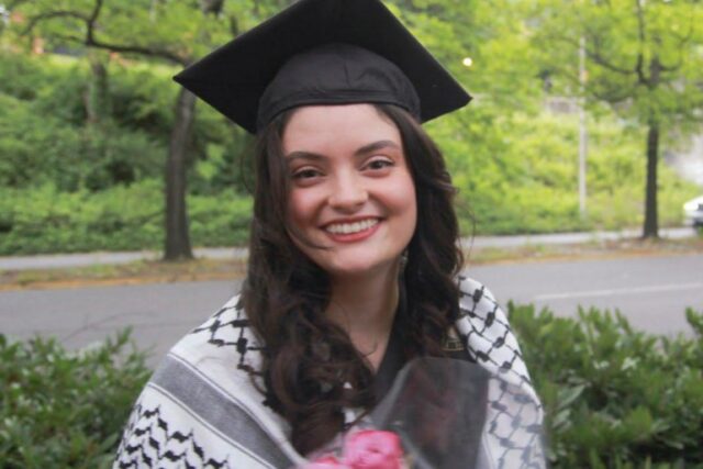 uma mulher com chapéu de formatura e keffiyeh sorrindo