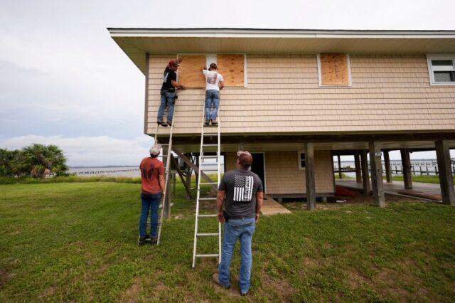 Jerry McCullen, no topo da escada à esquerda, e Carson Baze, no topo da escada à direita, colocaram madeira compensada nas janelas de uma casa antes do furacão Helene, que deverá atingir a costa na noite de quinta-feira, em Alligator Point, Flórida, quarta-feira, 25 de setembro de 2024 (Foto AP / Gerald Herbert)