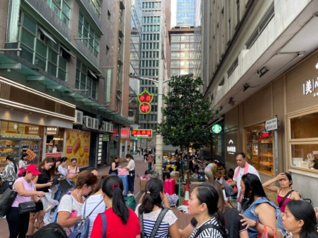 Mulheres reuniram-se numa rua pedonal no Distrito Central de Hong Kong. Existem edifícios altos em ambos os lados.