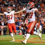 DENVER, CO - 1º DE OUTUBRO: O running back Kareem Hunt nº 27 do Kansas City Chiefs corre para a end zone com um touchdown no quarto período enquanto o tight end Travis Kelce nº 87 começa a comemorar no Broncos Stadium em Mile High em 1º de outubro de 2018 em Denver, Colorado.