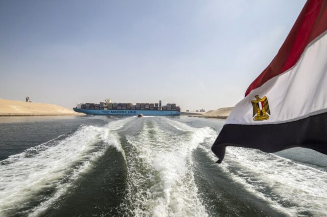 Uma bandeira nacional egípcia tremula em um barco enquanto mostra um navio porta-contêineres navegando na nova seção do Canal de Suez, na cidade portuária egípcia de Ismailia, 135 km a nordeste do Cairo, em 14 de outubro de 2019. - Desde que o Canal de Suez foi inaugurado em meio à pompa e cerimônia há 150 anos, tornou-se uma das vias navegáveis ​​mais importantes do mundo. Mas o seu aniversário só será comemorado discretamente no Egito.