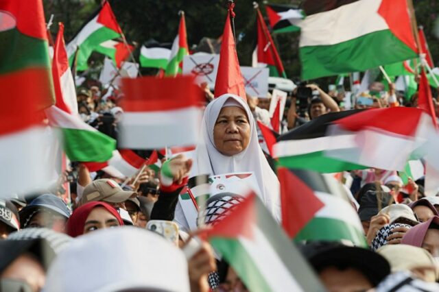 Uma mulher observa enquanto as pessoas levantam bandeiras palestinas durante um protesto contra Israel e em apoio aos palestinos do lado de fora da embaixada dos EUA em Jacarta, Indonésia, em 6 de outubro de 2024.