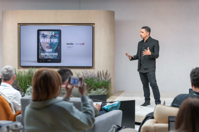 Panos Panay no palco no evento de lançamento do Kindle da Amazon em 2024, com uma tela grande à sua direita mostrando o novo Kindle Colorsoft e seu preço.