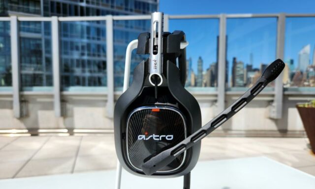 O headset para jogos Astro A40 TR fica em um suporte branco em uma mesa externa, com seu microfone embutido estendido.