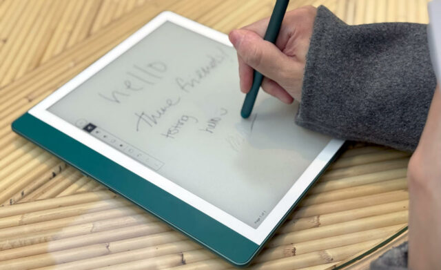 O Amazon Kindle Scribe em uma mesa, com uma mão segurando uma caneta na tela, apagando algumas palavras.